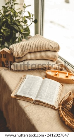 Cozy winter photo, stack of sweaters, open Bible, tea and candle.