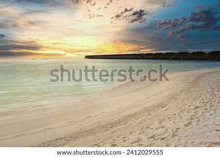 A pristine beach adorned with golden sands, kissed by the warm hues of a vibrant sunset. Colorful skies blend into the tranquil sea, casting a breathtaking spectacle. Nestled along the shore are charm Royalty-Free Stock Photo #2412029555