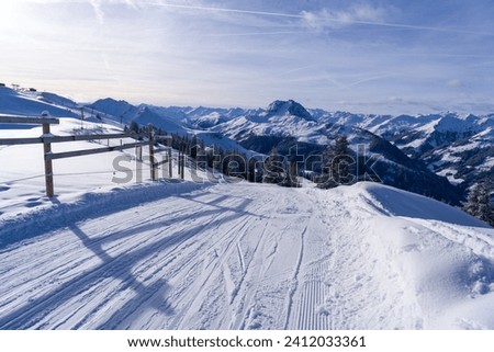 Groomed ski piste and white winter landscape with snowy trees mountains clouds and fresh powder snow taken at high altitude near Kirchberg and Kitzbuhel and the Brixental valley in the Austrian alps.