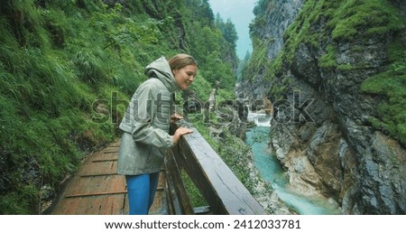 Woman enjoys the rain while hiking in a rocky gorge with mountain fast flowing river. Narrow wooden staircase along the canyon in Austria. Royalty-Free Stock Photo #2412033781