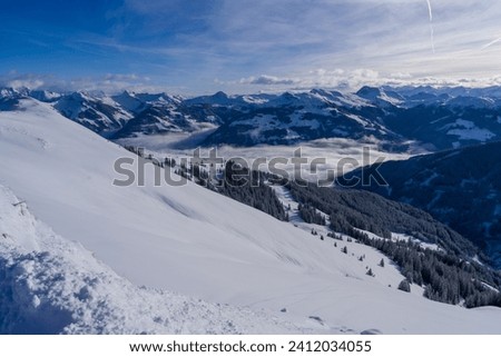 Scenic white winter landscape with mountains, clouds down in the valley and fresh powder snow taken at high altitude near Kirchberg and Kitzbuhel and the Brixental valley in the Austrian alps.
