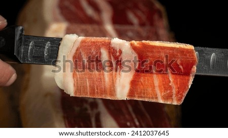 Delicious slice of authentic Iberian ham from Spain from genetically pure Iberian pigs cut with a knife by a professional for tasting Royalty-Free Stock Photo #2412037645