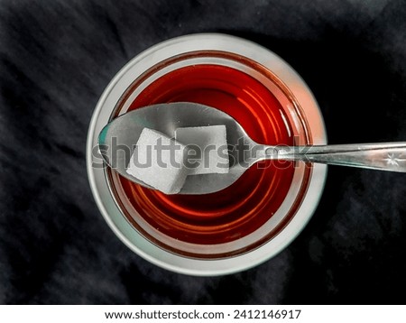 Sugar cubes on a teaspoon with a cup of tea on a black cloth background Royalty-Free Stock Photo #2412146917