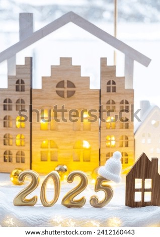 Golden figures number 2025 and tiny home on background of cozy windows of a house with warm light with festive decor of stars,snow and garlands. Greeting card, Happy New Year, cozy home