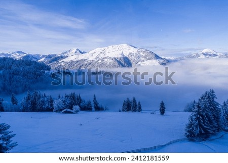 Winter wonderland snow covered field and mountain landscape. Clouds on valley floor on beautiful clear sunny blue bird day after fresh snowfall.  Austrian alps, Brixental, Kirchberg and Kitzbuhel.