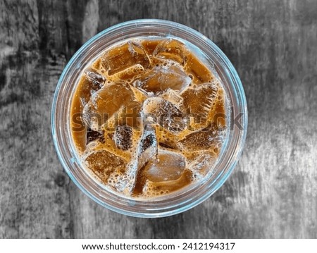 Picture of a gray wooden floor and a clear white glass with chunks of ice and tea with fresh milk, a light orange color, a drink that tastes delicious and has the aroma of tea.