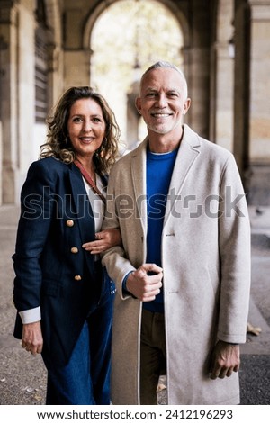 Affectionate senior man and woman standing happy and relaxed in old town. Mature couple bonding together in looking at camera and holding arms.