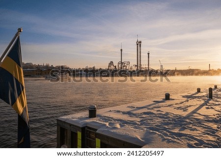 Fuming sea, sea smoke, in Stockholm due to an arctic cold blast, the amusement park of Grona lund in the background, sunshine and snow. A commuter ferry boat passing by. Royalty-Free Stock Photo #2412205497