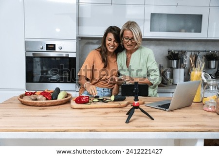 Grandma and daughter record a cooking vlog or podcast while chopping vegetables for a healthy vegetarian meal in the kitchen and stream it online. Vegan food preparation