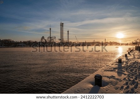 Fuming sea, sea smoke, in Stockholm due to an arctic cold blast, the amusement park of Grona lund in the background, sunshine and snow. Royalty-Free Stock Photo #2412222703