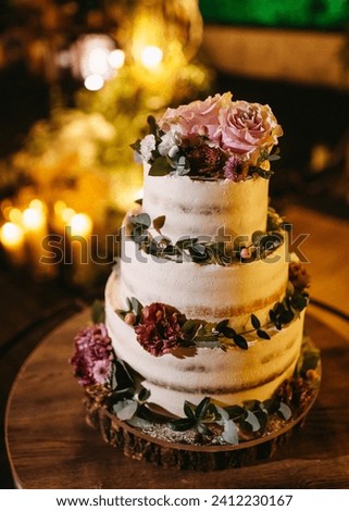 A three-tiered wedding cake adorned with fresh flowers and greenery, set against a backdrop of warm candlelight. Royalty-Free Stock Photo #2412230167