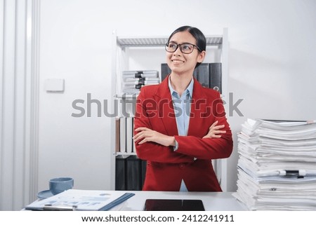 cheerful individual wearing glasses and a red blazer, hard working with large stack of papers, working on a balance sheet for yearly taxes.