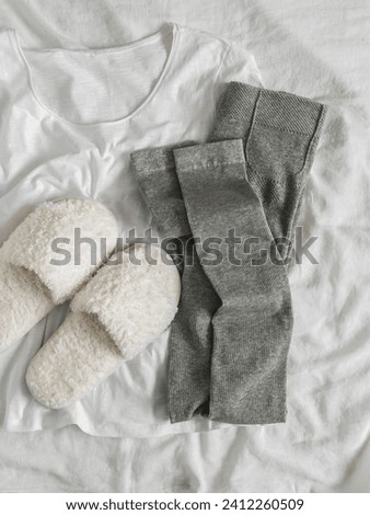 Comfortable women's home clothes - ribbed cotton leggings, white T-shirt, soft fur slippers on a light background, top view