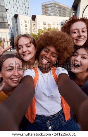 Happy multiracial group of female friends taking a funny selfie with a smartphone. Cheerful young women gathering together using phone to take photos looking at camera. Vertical social media image.