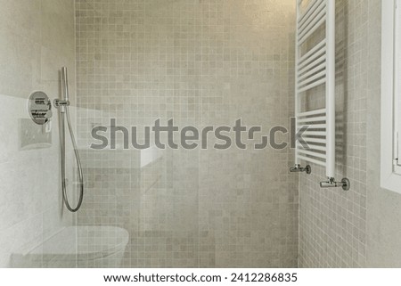 Shower cabin with tempered glass screen, wall-mounted towel radiator, chrome taps and modern cream-coloured tiles Royalty-Free Stock Photo #2412286835