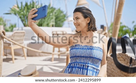 Young hispanic woman taking a selfie picture sitting on the table at sunny restaurant terrace