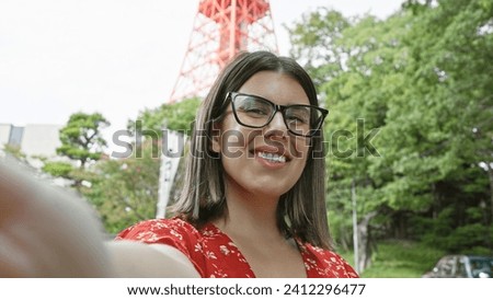 Beautiful hispanic woman in glasses, enjoying her tokyo travel adventure, takes cheery selfie at famous tokyo tower spot