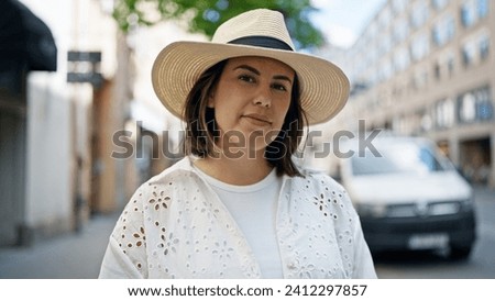 Beautiful young hispanic woman standing with serious expression looking a the camera wearing summer hat in the streets of Stockholm Royalty-Free Stock Photo #2412297857
