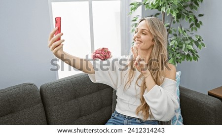 Smiling young woman taking a selfie with a phone in a cozy indoor living room.