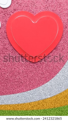 red cardboard paper cut into heart shape and glitter paper with pink, grey, yellow, green color background on vertical frame