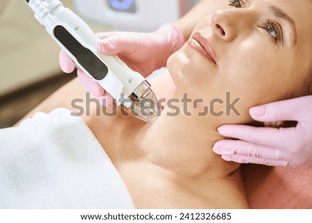 Close up of cosmetologist doing microneedle rf lifting of neck skin of woman Royalty-Free Stock Photo #2412326685