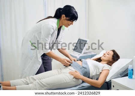 Female gynecologist preparing belly of young caucasian pregnant woman for ecg