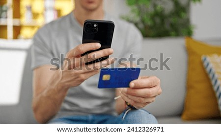 Young hispanic man make photo to credit card by smartphone at home