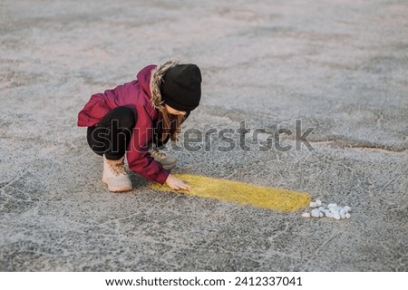 Little diligent lonely girl, a child draws a drawing with colored chalk on the asphalt outdoors on the street in the park. Photography, close-up portrait, design, childhood concept.