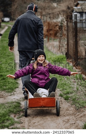 A strong man, father, grandfather rides, carries on a rusty old cart, wagon along the road in the village, countryside, a small beautiful smiling, happy girl, child. Photography, close-up portrait.