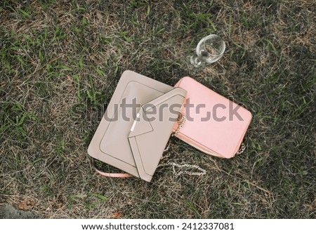 Two leather handbags with a glass of champagne lie on the green grass at a holiday party. Photography, style, fashion, copy space.c