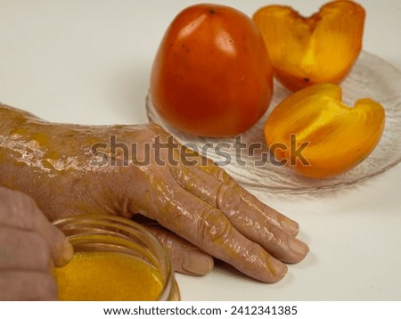 An elderly woman applies an anti-aging mask made from fresh persimmon pulp to her hand