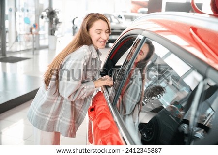 Cheerful woman standing her new automobile in dealership enjoying purchase