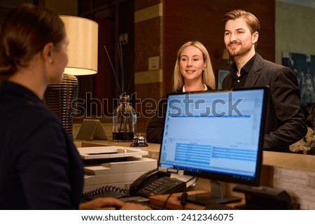 Receptionist typing on computer while couple standing at reception desk Royalty-Free Stock Photo #2412346075