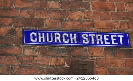 Street name sign: Blue wall plaque on a red brick wall with Church Street is white capital letters. A location is centre of Ross on Wye in Herefordshire, England.