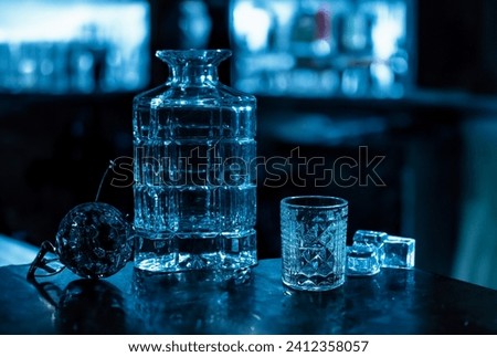Empty decander bottle for vodka and glasses on dark background in night club.