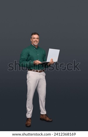Happy middle aged business man ceo wearing green shirt standing isolated on gray using laptop. Smiling mature businessman professional executive manager looking at camera holding computer. Full body