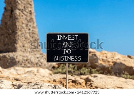 Invest and do business symbol. Concept word Invest and do business on beautiful black chalk blackboard. Beautiful red stone blue sky background. Invest and do business concept. Copy space.
