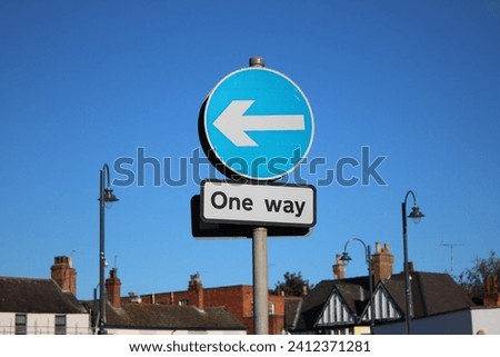 UK circular one way sign attached to a pole, blue sky and houses in background blurred