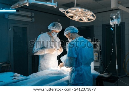 Rear view of team of professional surgeons performing invasive surgery on patient lying in hospital operating room. Surgeons using instruments. Dark and cold atmosphere. Concept of emergency.