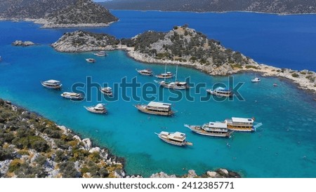 Excursion boats take a swimming break in Aquarium Bay Kekova in Turkey. Cinematic drone shot flying over a beautiful bay with turquoise water and tour boats. Aerial view of many motorboats  Royalty-Free Stock Photo #2412385771