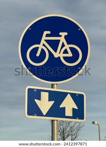 Blue road sign indicating a bike, Bike path road sign. Traffic sign white bicycle on blue circle against the backdrop of trees and sky. Concept of infrastructure development for ecological transport.