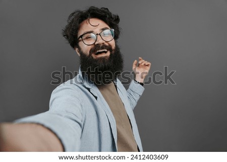 Delighted bearded man in casual wear taking a selfie, laughing and enjoying the moment, dark background