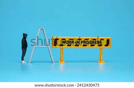 A picture of miniature men, ladder and work in progress sign. 