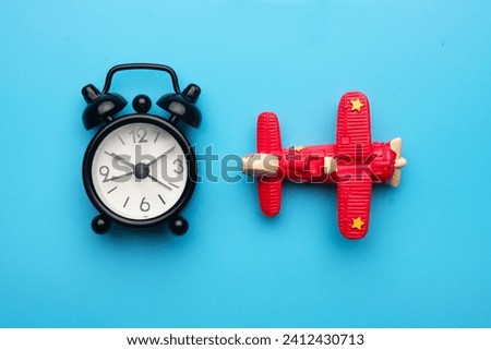 A flatlay picture of toy aeroplane and alarm clock on blue background. Flight time concept.