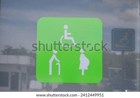 White sign of old man pregnant and wheelchair on light green square label on glass door of public toilet, Thailand. 