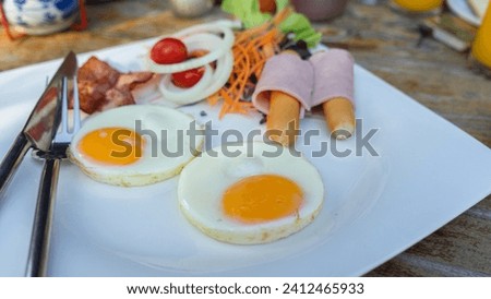 Picture of the hotel's breakfast set, with fried eggs, bacon, ham, and sausage arranged on a white porcelain plate. There are knives and forks placed ready to eat.