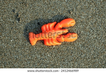 Exterior to pview close up photo of a plastic toy mold of a lobster in orange colour in cartoon style for kids to play on the sand at the beach