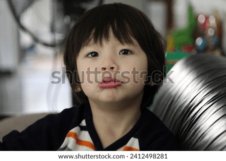 Interior photo portrait of a 3 years old young baby kid child children male cheeky boy who is doing a funny face to the photographer