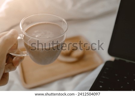 Image of woman hand holding and drinking coffee, milk tea cup while working and using laptop on white bed, freelancer lifestyle.