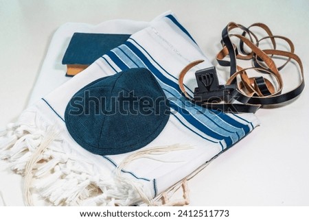 On the table is a tallit (a man's prayer shawl), a kippah, a siddur, and a head tefillin with the letter shin (hebrew). Religious jewish traditions (113) Royalty-Free Stock Photo #2412511773